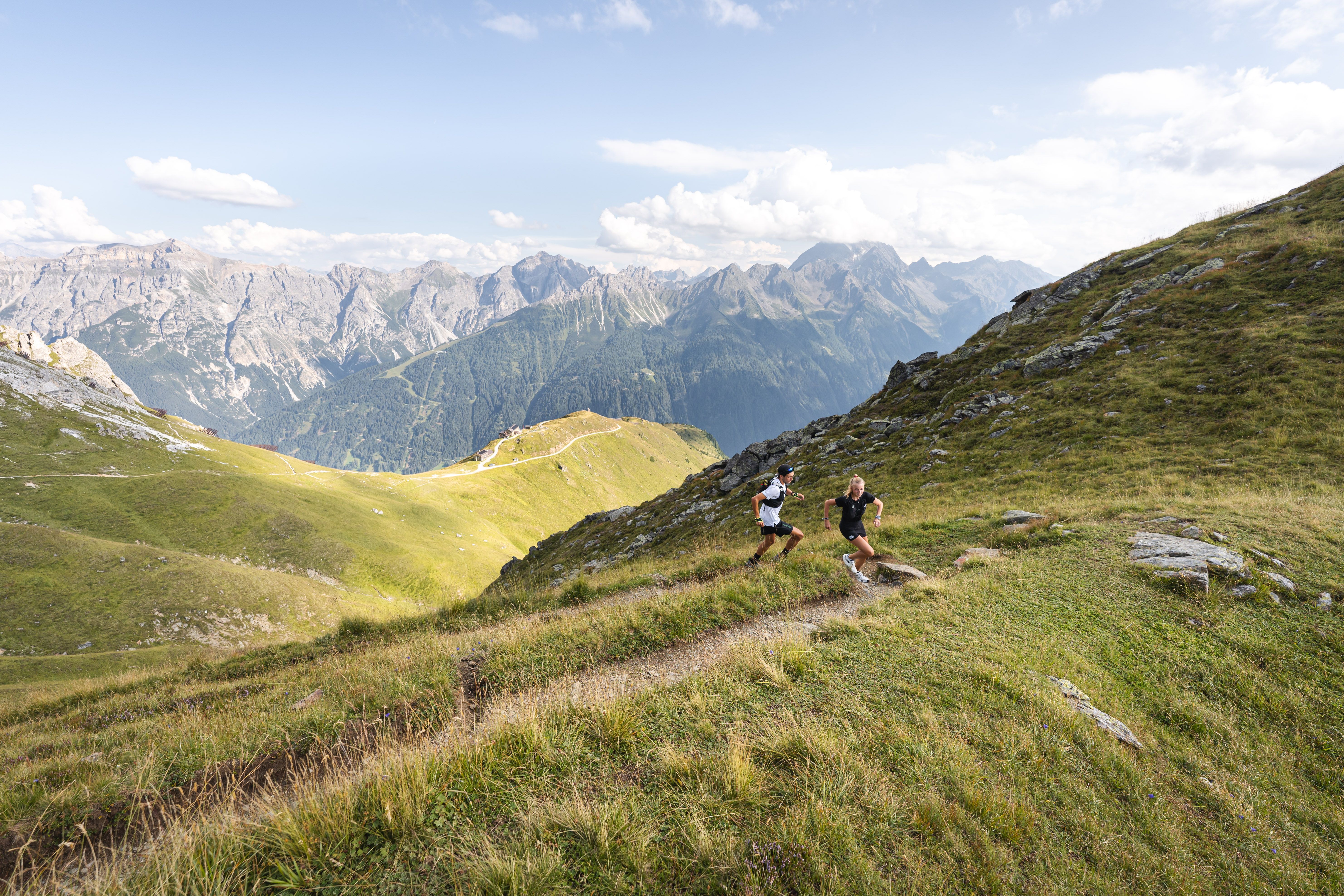 Landschaftsbild von Neustift im Stubaital mit zwei Personen, die einen Trail hinauf laufen.